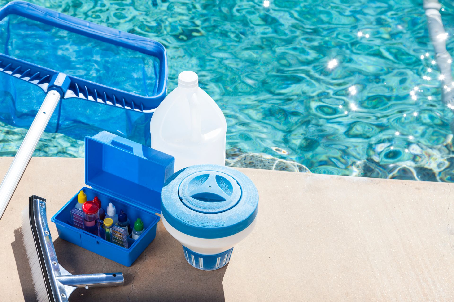 Pool maintenance tools including a skimmer net, water testing kit, and floating chlorine dispenser by a clean swimming pool in Waterloo.